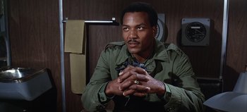 Movie still from “Ice Station Zebra” (1968), directed by John Sturges – A man sitting in front of a wooden wall holding a mouse; Close Up shot, Low angle