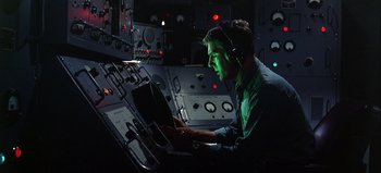 Movie still from “Ice Station Zebra” (1968), directed by John Sturges – A man with headphones is working on a computer; Medium shot, Low angle