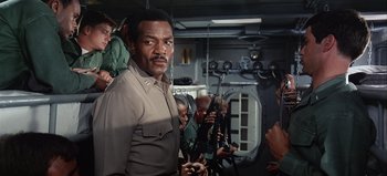Movie still from “Ice Station Zebra” (1968), directed by John Sturges – A group of people standing in a room with guns; Medium shot, Low angle