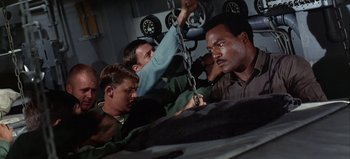 Movie still from “Ice Station Zebra” (1968), directed by John Sturges – A group of men standing next to each other in a garage; Medium shot, High angle