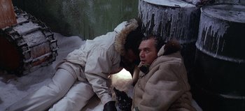 Movie still from “Ice Station Zebra” (1968), directed by John Sturges – A man in winter clothes is laying on the ground; Medium shot, High angle