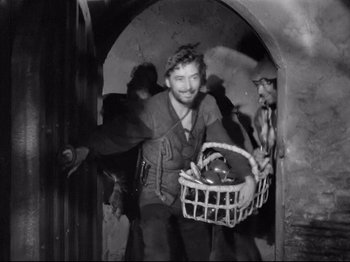 Movie still from “If I Were King” (1938), directed by Frank Lloyd – A man holding a basket of food in a doorway; Medium shot, High angle
