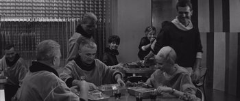 Movie still from “Voyage to the End of the Universe” (1963), directed by Jindrich Polák – A group of people sitting at a table eating food; Medium shot, Over the shoulder angle
