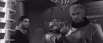 Movie still from “Voyage to the End of the Universe” (1963), directed by Jindrich Polák – An older man holding up two fingers in front of a robot; Medium shot, Low angle