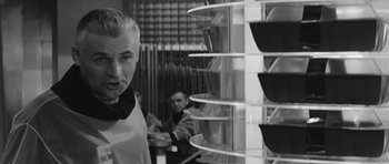 Movie still from “Voyage to the End of the Universe” (1963), directed by Jindrich Polák – A man standing in front of a shelf of bowls; Close Up shot, Low angle