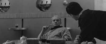 Movie still from “Voyage to the End of the Universe” (1963), directed by Jindrich Polák – A black and white photo of a man sitting in front of a mirror; Medium shot, Over the shoulder angle
