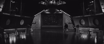 Movie still from “Voyage to the End of the Universe” (1963), directed by Jindrich Polák – A black and white photo of a room with a person standing in front; Extreme Wide shot, High angle