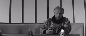 Movie still from “Voyage to the End of the Universe” (1963), directed by Jindrich Polák – An older man sitting at a table holding a cell phone; Close Up shot, Low angle