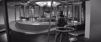 Movie still from “Voyage to the End of the Universe” (1963), directed by Jindrich Polák – A black and white photo of a man and a woman in a room; Wide shot, High angle