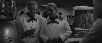 Movie still from “Voyage to the End of the Universe” (1963), directed by Jindrich Polák – Two men in white shirts and black ties holding drinks; Medium shot, Over the shoulder angle