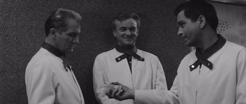 Movie still from “Voyage to the End of the Universe” (1963), directed by Jindrich Polák – A man holding a cell phone while standing next to two other men; Medium shot, Low angle
