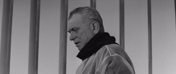 Movie still from “Voyage to the End of the Universe” (1963), directed by Jindrich Polák – An older man wearing a jacket and standing in front of a fence; Close Up shot, Low angle