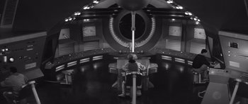 Movie still from “Voyage to the End of the Universe” (1963), directed by Jindrich Polák – A man sitting in a chair in front of a large screen; Wide shot, High angle