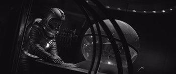 Movie still from “Voyage to the End of the Universe” (1963), directed by Jindrich Polák – A man in a space suit working on a computer in front of an orbiter; Medium shot, Low angle