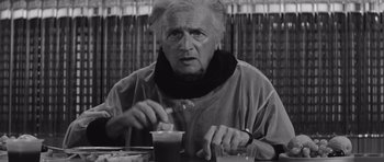 Movie still from “Voyage to the End of the Universe” (1963), directed by Jindrich Polák – An older man sitting at a table with a bowl of soup; Close Up shot, Low angle