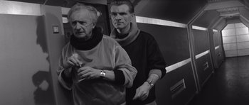 Movie still from “Voyage to the End of the Universe” (1963), directed by Jindrich Polák – Two men standing next to each other in front of a wall; Medium shot, Over the shoulder angle