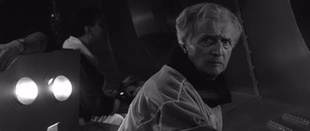 Movie still from “Voyage to the End of the Universe” (1963), directed by Jindrich Polák – An older man sitting in the back of a vehicle; Medium shot, Low angle