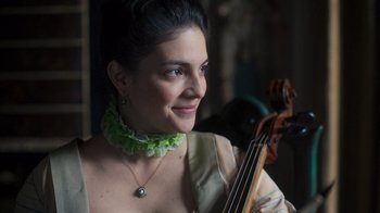 Movie still from “The Bohemian” (2022), directed by Petr Václav – A woman in a green necklace holding a violin; Close Up shot, High angle