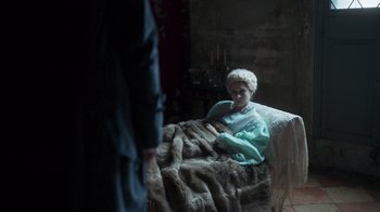 Movie still from “The Bohemian” (2022), directed by Petr Václav – An older woman sitting on a couch in a room; Wide shot, High angle