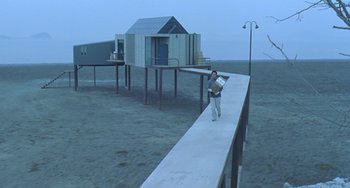 Movie still from “Il Mare” (2000), directed by Hyun-seung Lee – A person standing on a pier holding a book; Extreme Wide shot, High angle