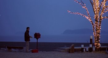 Movie still from “Il Mare” (2000), directed by Hyun-seung Lee – A man standing on a beach next to an umbrella; Extreme Wide shot, High angle