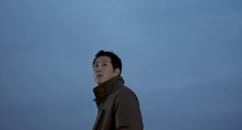 Movie still from “Il Mare” (2000), directed by Hyun-seung Lee – A man in a brown jacket standing in front of a blue sky; Close Up shot, Low angle