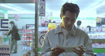 Movie still from “Il Mare” (2000), directed by Hyun-seung Lee – A man is looking down at a piece of paper; Medium shot, Low angle
