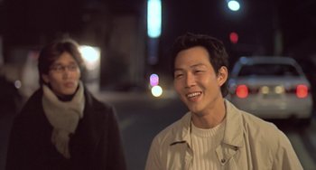 Movie still from “Il Mare” (2000), directed by Hyun-seung Lee – A man standing next to another man on a street; Close Up shot, Over the shoulder angle