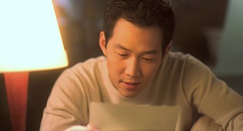 Movie still from “Il Mare” (2000), directed by Hyun-seung Lee – A man sitting at a table looking down at a piece of paper; Close Up shot, Over the shoulder angle