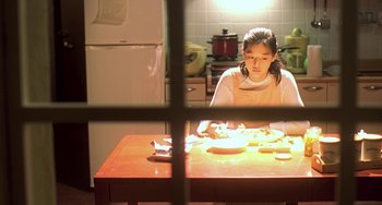 Movie still from “Il Mare” (2000), directed by Hyun-seung Lee – A girl sitting at a table in a kitchen preparing food; Medium shot, Over the shoulder angle