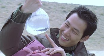 Movie still from “Il Mare” (2000), directed by Hyun-seung Lee – A man holding a bag and smiling at the camera; Close Up shot, Over the shoulder angle