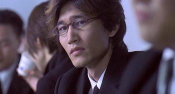 Movie still from “Il Mare” (2000), directed by Hyun-seung Lee – A person wearing a suit and glasses; Close Up shot, Over the shoulder angle