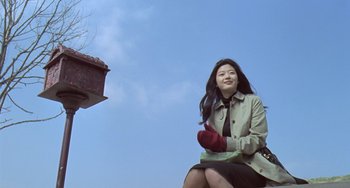 Movie still from “Il Mare” (2000), directed by Hyun-seung Lee – A woman sitting on the ground with a bird in her hand; Wide shot, Low angle