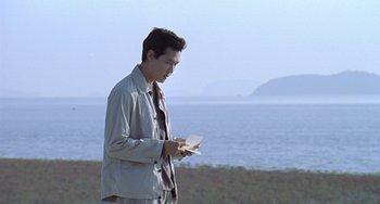 Movie still from “Il Mare” (2000), directed by Hyun-seung Lee – A man standing by the water holding a paper; Medium shot, Low angle