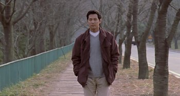 Movie still from “Il Mare” (2000), directed by Hyun-seung Lee – A man standing on a path in a wooded area; Medium shot, Low angle