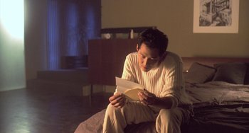 Movie still from “Il Mare” (2000), directed by Hyun-seung Lee – A man sitting on the floor reading a letter; Medium shot, Over the shoulder angle