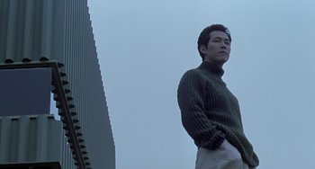 Movie still from “Il Mare” (2000), directed by Hyun-seung Lee – A man standing in front of a building with his hands in his pockets; Medium shot, Low angle