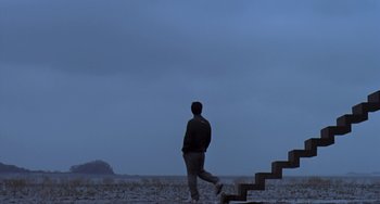 Movie still from “Il Mare” (2000), directed by Hyun-seung Lee – A man walking up a set of stairs in the middle of a field; Extreme Wide shot, Low angle