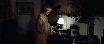 Movie still from “Images” (1972), directed by Robert Altman – A woman standing in front of a table with a lamp; Medium shot, High angle