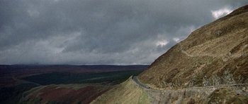 Movie still from “Images” (1972), directed by Robert Altman – A car driving down the side of a road on top of a hill; Extreme Wide shot, High angle
