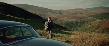 Movie still from “Images” (1972), directed by Robert Altman – A man walking up a hill near a car; Wide shot, High angle