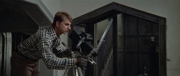 Movie still from “Images” (1972), directed by Robert Altman – A man is holding a camera and a sword; Medium shot, Low angle