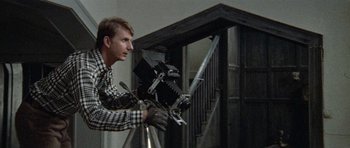 Movie still from “Images” (1972), directed by Robert Altman – A man holding a camera in front of a staircase; Medium shot, Low angle