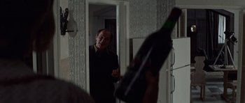 Movie still from “Images” (1972), directed by Robert Altman – A man standing in front of a mirror holding a wine bottle; Medium shot, Over the shoulder angle