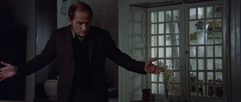 Movie still from “Images” (1972), directed by Robert Altman – A man in a black suit is holding out his hand; Medium shot, Over the shoulder angle