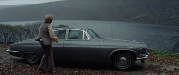 Movie still from “Images” (1972), directed by Robert Altman – A woman standing in front of a car near a body of water; Wide shot, Low angle