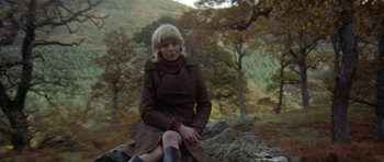 Movie still from “Images” (1972), directed by Robert Altman – A woman sitting on top of a rock in a wooded area; Wide shot, Low angle
