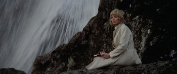 Movie still from “Images” (1972), directed by Robert Altman – A woman sitting on a rock near a waterfall; Medium shot, Low angle