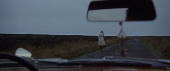 Movie still from “Images” (1972), directed by Robert Altman – A woman walking down a road with a car in the background; Wide shot, High angle