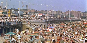 Movie still from “Imitation of Life” (1959), directed by Douglas Sirk – A crowd of people on a beach near a pier; Extreme Wide shot, High angle